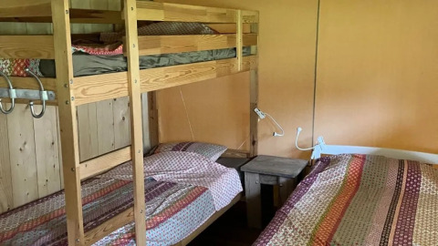 Das Foto zeigt den Schlafbereich eines Safarizeltes mit Badezimmer, mit Etagenbett und Einzelbett.