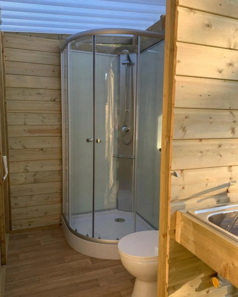 Holzverkleidetes Badezimmer im Safarizelt mit moderner Dusche, WC und Spülbecken, natürlich beleuchtet