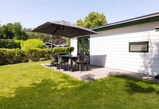 Lodge mit Terrasse, Esstisch, Stühlen und großem Sonnenschirm auf grüner Wiese bei White Lodge im Sommer.