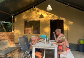 Family dining together outside at a table in front of a safari tent surrounded by nature in summer.