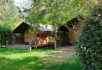 Dos tiendas safari en el camping La Digue en Francia, rodeadas de vegetación y árboles bajo el sol.