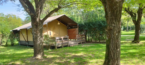 Safari tent at Campsite La Digue in France, set among trees and grass on a bright sunny day.