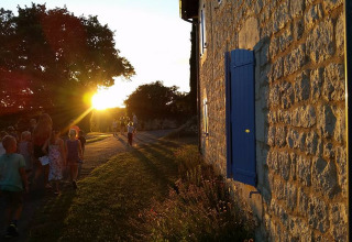 Bambini e adulti passeggiano al tramonto accanto a un edificio in pietra con persiane blu in Occitania, Francia.