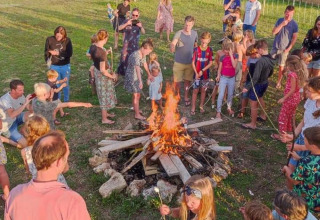 Gruppo di persone che arrostiscono marshmallow intorno a un falò presso il campeggio Camp Redon in Occitanie.