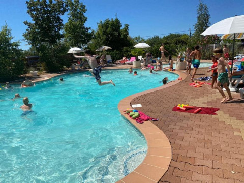 Bambini e adulti si divertono giocando e nuotando nella piscina del Camp Redon in una giornata di sole in Occitania, Francia.