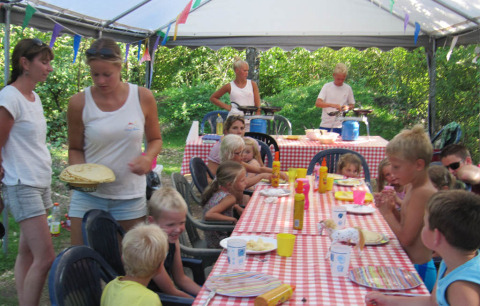 Bambini e adulti condividono un pasto sotto una tenda al campeggio Camp Redon in Occitania, Francia.