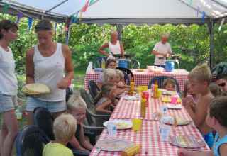 Bambini e adulti condividono un pasto sotto una tenda al campeggio Camp Redon in Occitania, Francia.