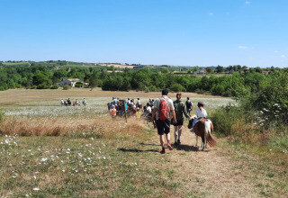 Persone camminano attraverso un prato panoramico al campeggio Camp Redon, Occitania, Francia.