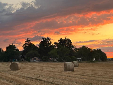 Campo con rotoballe e tende sotto un tramonto al campeggio Camp Redon in Occitania, Francia.