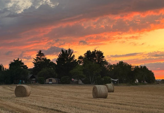 Campo con rotoballe e tende sotto un tramonto al campeggio Camp Redon in Occitania, Francia.
