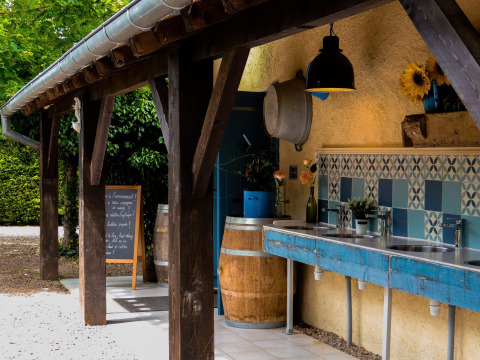 Zona lavaggio all’aperto con piastrelle blu, botti e travi in legno presso il Camp Redon in Occitania, Francia.