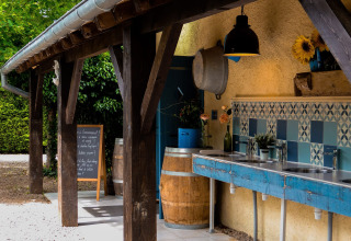 Zona lavaggio all’aperto con piastrelle blu, botti e travi in legno presso il Camp Redon in Occitania, Francia.