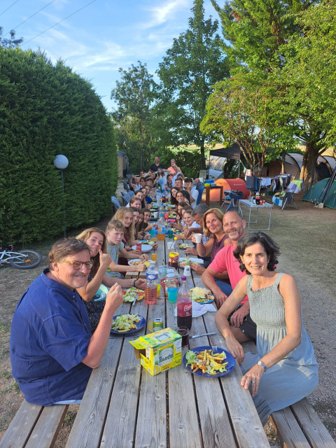 Grande gruppo di persone che mangia insieme a un lungo tavolo all'aperto al campeggio Camp Redon in Francia.