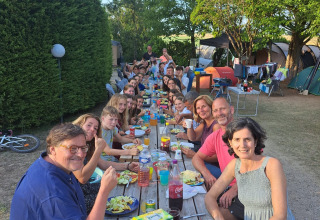 Grande gruppo di persone che mangia insieme a un lungo tavolo all'aperto al campeggio Camp Redon in Francia.