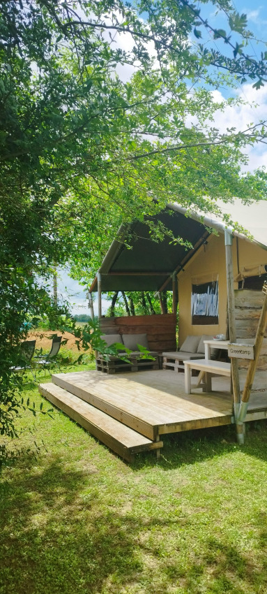 Safari tent at Campsite Camp Redon in France with a wooden deck, outdoor seating, and lush greenery.