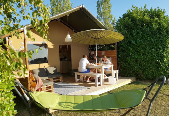 Een gezin zit aan een tafel bij een Safaritent, met een groene hangmat op de voorgrond.