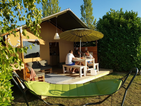 Une famille est assise à une table devant une tente safari, avec un hamac vert au premier plan.