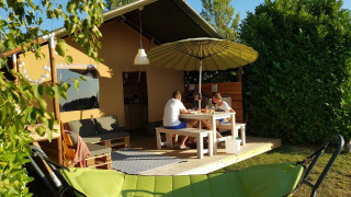 A family is sitting at a table outside a Safaritent, with a green hammock in the foreground.