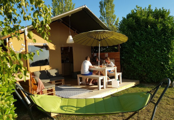 A family is sitting at a table outside a Safaritent, with a green hammock in the foreground.