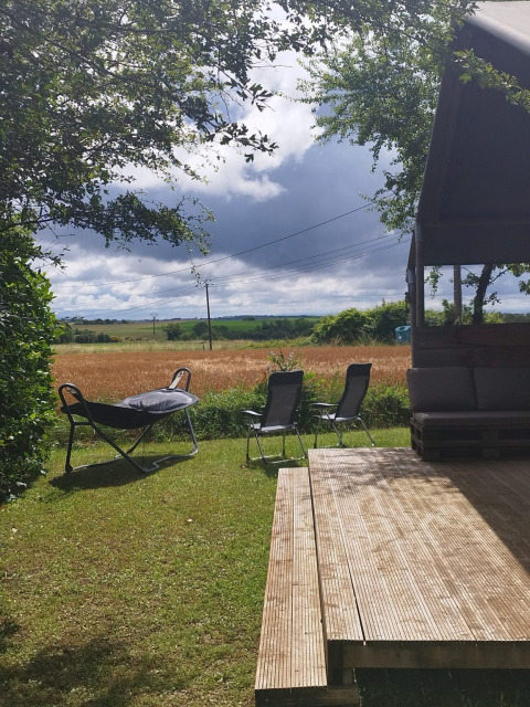 View from Safaritent at Campsite Camp Redon in France featuring a wooden deck, chairs, and open fields.