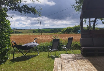View from Safaritent at Campsite Camp Redon in France featuring a wooden deck, chairs, and open fields.