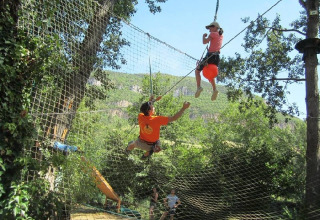 Bambini giocano su una rete da arrampicata sospesa al campeggio Camp Redon, parco vacanze in Occitania, Francia.