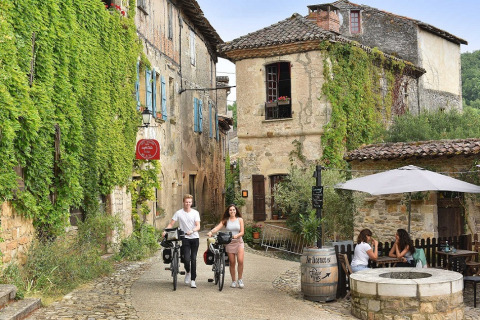 Scorcio pittoresco a Camp Redon, Occitanie, Francia, con ciclisti e persone che si rilassano al caffè.