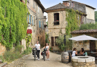 Scorcio pittoresco a Camp Redon, Occitanie, Francia, con ciclisti e persone che si rilassano al caffè.