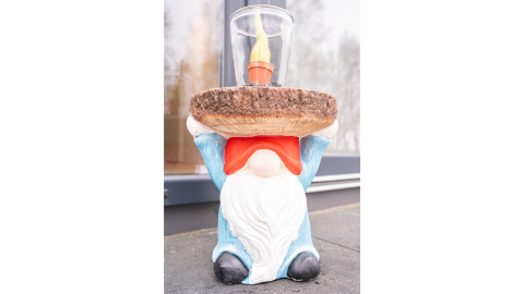 Statua da giardino di gnomo con cappello rosso che regge un vassoio e candela a Villa BushBush, De Kremmer, Paesi Bassi.