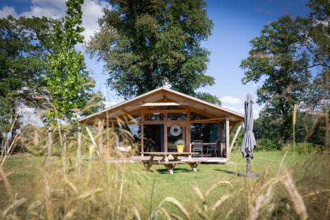 Foto der Wellness Luxe Lodge, eine gemütliche Holzhütte mit Terrasse im Grünen, umgeben von Bäumen.