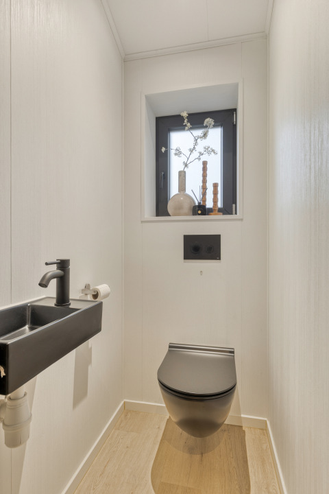 Aseo moderno con inodoro negro suspendido, pequeño lavabo y decoración en la ventana en el Weideblik lodge.