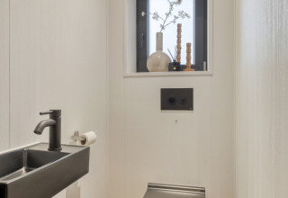 Moderne toilet med sort væghængt toilet, lille vask og dekoration i vinduet i Weideblik-lodgen.