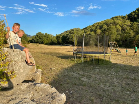 Due bambini seduti su una roccia vicino a un'area giochi con trampolino al campeggio Le Moulin de Cost, Francia.