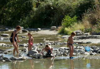 Famiglia che gioca in un fiume poco profondo al campeggio Le Moulin de Cost, in Auvergne-Rhône-Alpes, Francia.