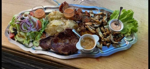 Grande vassoio con bistecca, patate, insalata, salse e verdure grigliate su un tavolo di legno.