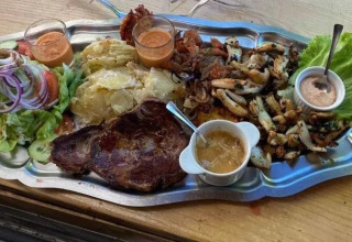 Grande vassoio con bistecca, patate, insalata, salse e verdure grigliate su un tavolo di legno.