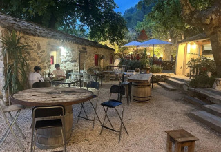 Area esterna accogliente con edifici in pietra e tavoli rustici al campeggio Le Moulin de Cost.