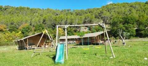 Parco giochi con altalene e scivolo davanti a tende safari al campeggio Le Moulin de Cost in Alvernia-Rodano-Alpi.