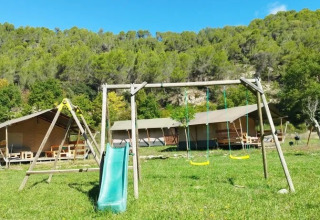 Parco giochi con altalene e scivolo davanti a tende safari al campeggio Le Moulin de Cost in Alvernia-Rodano-Alpi.