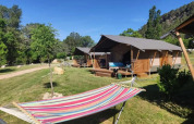 Safari-Zelte mit Veranda und bunter Hängematte davor, eingebettet in Wiese und Bäume bei blauem Himmel.