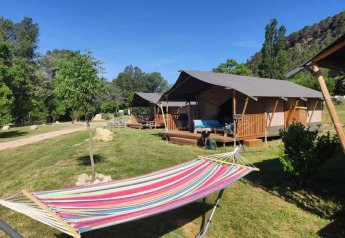 Safari-Zelte mit Veranda und bunter Hängematte davor, eingebettet in Wiese und Bäume bei blauem Himmel.