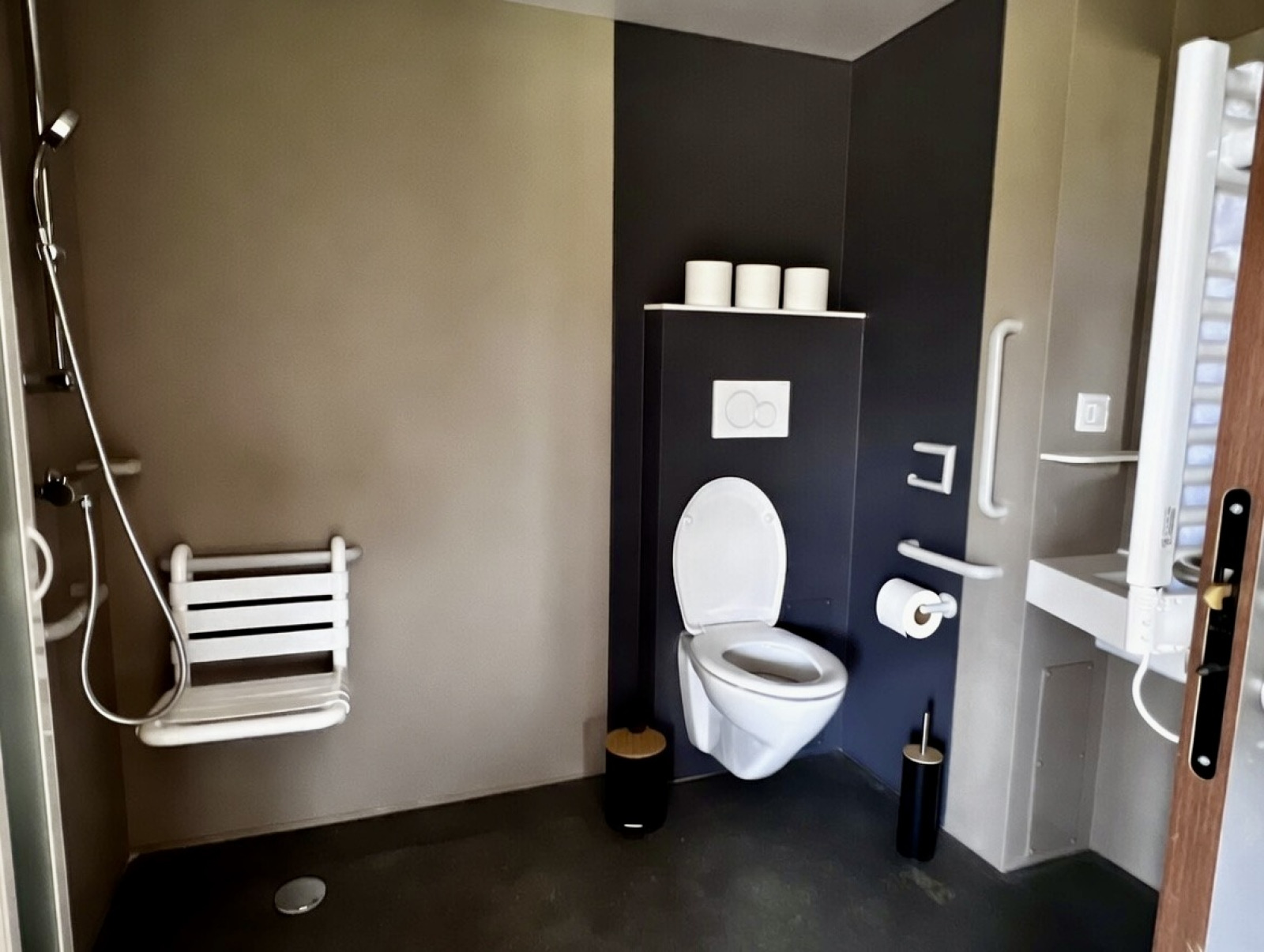 Toegankelijke badkamer in Cabane Spa Dieren, Domaine des Feuilles, Frankrijk, met douchestoel en beugels.