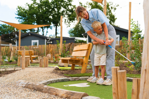 Eine Frau hilft einem Jungen beim Minigolfspielen an der Eco Boslodge Jacuzzi, Estate De IJsvogel, Niederlande.