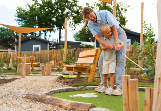 A woman helps a young boy play minigolf at Eco Boslodge Jacuzzi, Estate De IJsvogel in the Netherlands.