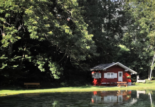 Charmante cabane rouge près d’un étang paisible, dans la verdure d’Austriaparks Camping Arlberg, Tyrol, Autriche.