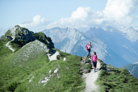 Two hikers in pink jackets walk along a mountain trail near Pettneu am Arlberg with the Alps behind them.