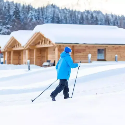 Iemand langlauft voor houten huisjes bij Austriaparks Camping Arlberg, Tirol, Oostenrijk onder een sneeuwlaag.