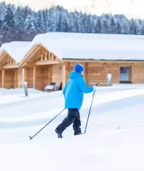 Persona che fa sci di fondo davanti a chalet in legno ad Austriaparks Camping Arlberg, Tirolo, Austria.