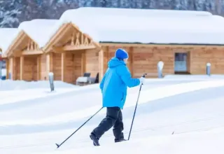 Personne faisant du ski de fond devant des chalets en bois à Austriaparks Camping Arlberg, Tyrol, Autriche.