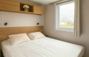 Camera da letto moderna con letto matrimoniale, finestra e mensola in legno al Vakantiehuis Celestia, Camping Papillon.
